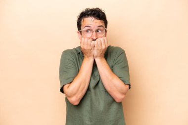 Beyazlı genç bir adam bej arka planda izole edilmiş gergin ve korkmuş bir şekilde elleriyle suni teneffüs yapıyor.