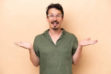 Young caucasian man isolated on beige background with shocked facial expression