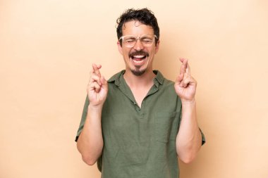 Beyazlı genç adam bej arka planda izole edilmiş ve şans diliyor.