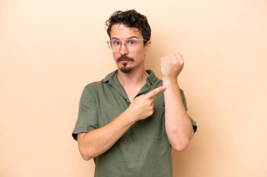 Young caucasian man isolated on beige background making the gesture of being late