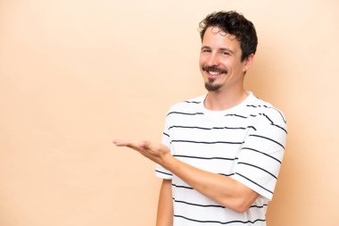 Beyazlı genç bir adam bej arka planda izole edilmiş bir şekilde gülümserken bir fikir sunuyor.
