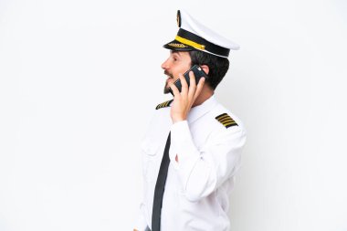 Beyaz arka planda izole edilmiş Kafkasyalı uçak pilotu cep telefonuyla birileriyle sohbet ediyor.