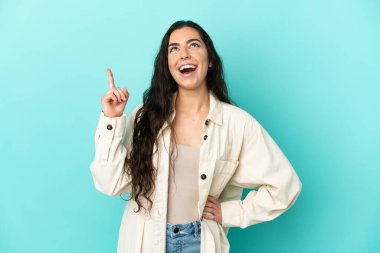 Mavi arka planda izole edilmiş genç beyaz kadın yukarı bakıyor ve şaşırıyor.