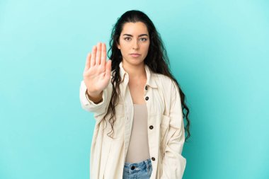 Mavi arka planda izole edilmiş genç beyaz kadın dur hareketi yapıyor.