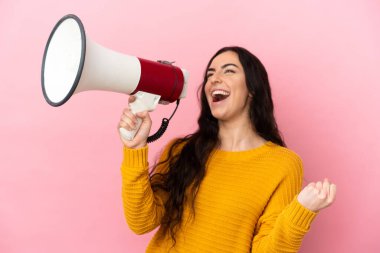 Pembe arka planda izole edilmiş genç beyaz bir kadın megafondan bir şey duyurmak için bağırıyor.