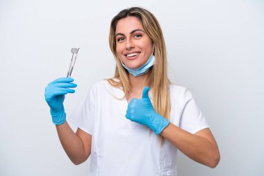 Beyaz arka planda izole edilmiş aletleri tutan dişçi kadın baş parmak hareketi yapıyor