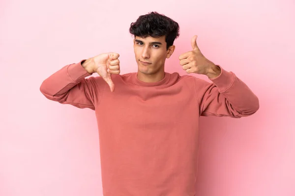 Young Argentinian man isolated on pink background making good-bad sign. Undecided between yes or not