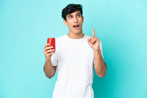 Young Argentinian man holding a refreshment isolated on blue background thinking an idea pointing the finger up