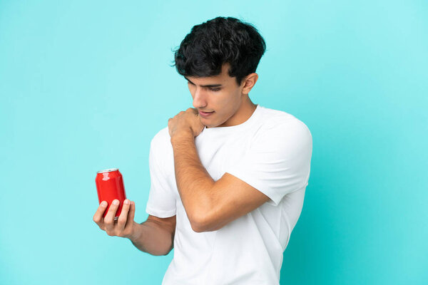 Young Argentinian man holding a refreshment isolated on blue background suffering from pain in shoulder for having made an effort