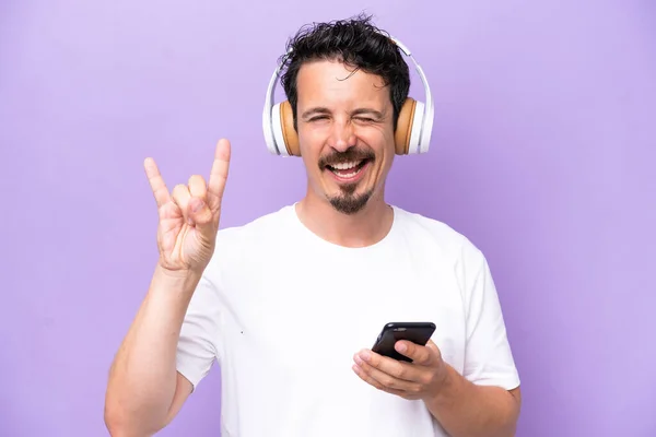 Jovem Caucasiano Isolado Fundo Roxo Ouvindo Música Com Gesto Rock — Fotografia de Stock