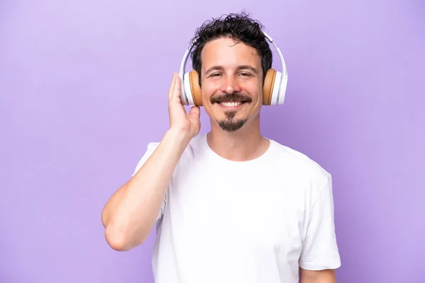 若いですCaucasian男隔離上の紫の背景リスニング音楽 — ストック写真