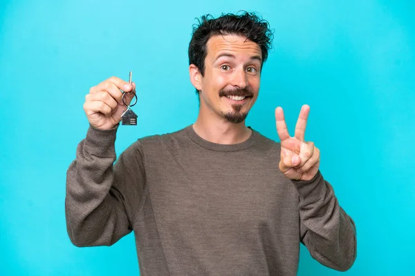 Young Caucasian Man Holding Home Keys Isolated Blue Background Smiling – stockfoto
