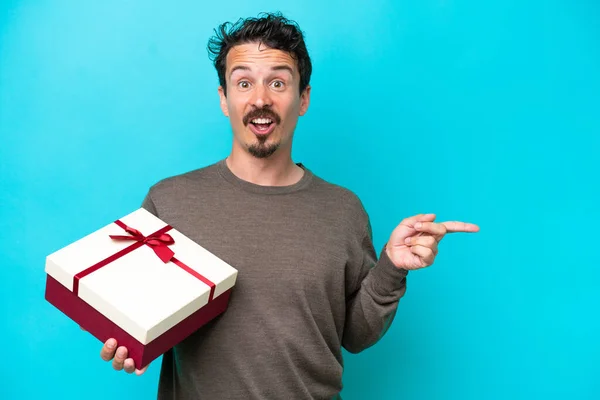 Young Man Holding Gift Surprised Pointing Finger Side — Stockfoto