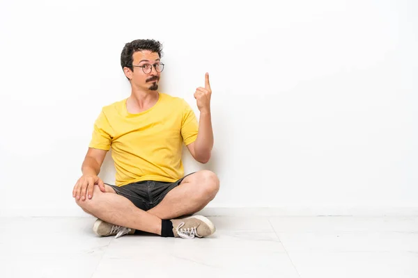 Joven Hombre Caucásico Sentado Suelo Aislado Sobre Fondo Blanco Señalando — Foto de Stock