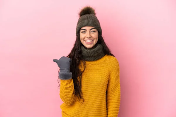 年轻的高加索女孩 头戴紫色背景的冬帽 指着侧面展示自己的产品 — 图库照片