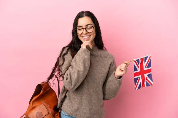 Young caucasian woman holding an United Kingdom flag isolated on pink background looking to the side and smiling