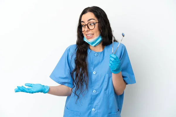 年轻的女牙医拿着被白色背景隔离的工具 面带微笑地看着一边 — 图库照片