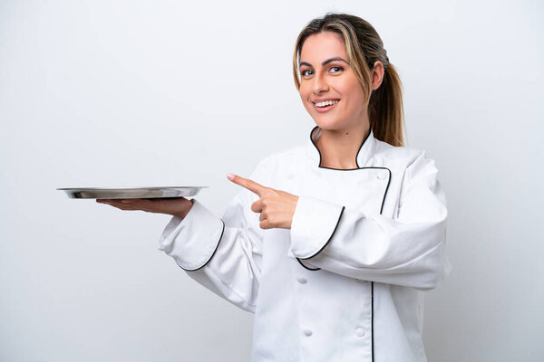 Young chef woman with tray isolated on white background pointing back