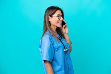 Mavi arka planda izole edilmiş orta yaşlı cerrah kadın cep telefonuyla sohbet ediyor.