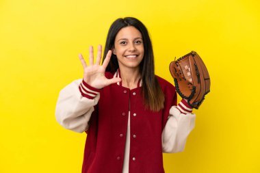 Beyzbol oynayan beyaz bir kadın sarı arka planda izole edilmiş, parmaklarıyla beşi sayıyor.