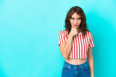 Kıvırcık saçlı genç bir kadın mavi arka planda izole edilmiş düşünüyor.