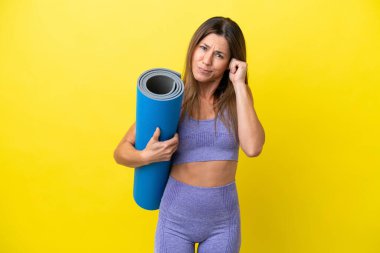 Sport woman going to yoga classes while holding a mat isolated non yellow background frustrated and covering ears