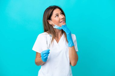 Middle age doctor woman isolated on blue background looking up while smiling