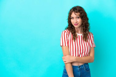 Kıvırcık saçlı genç bir kadın mavi arka planda yalnız gülüyor.