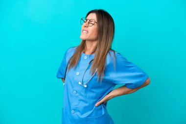 Orta yaşlı cerrah kadın, mavi arka planda izole edilmiş, gayret gösterdiği için sırt ağrısı çekiyor.