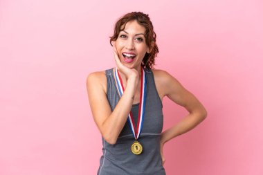 Pembe arka planda, şaşırmış ve şok olmuş yüz ifadesiyle madalyalı beyaz bir kadın.