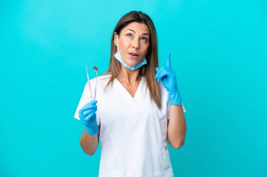 Middle age doctor woman isolated on blue background thinking an idea pointing the finger up