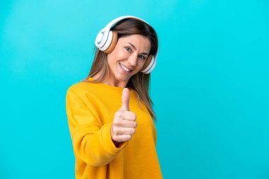 Middle age caucasian woman isolated on blue background listening music and with thumb up