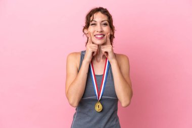 Pembe arka planda madalyalı beyaz bir kadın mutlu ve hoş bir ifadeyle gülümsüyor.