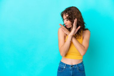 Mavi arka planda yalıtılmış kıvırcık saçlı genç bir kadın ellerini öne uzatıyor.