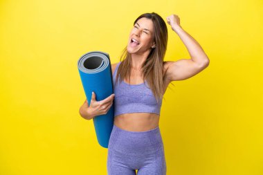 Spor kadını yoga derslerine giderken elinde sarı olmayan bir minder tutarak zaferi kutluyor.