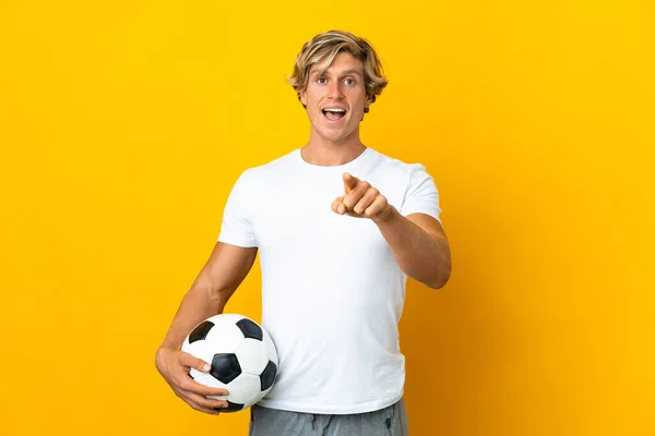 English football player over isolated yellow background surprised and pointing front