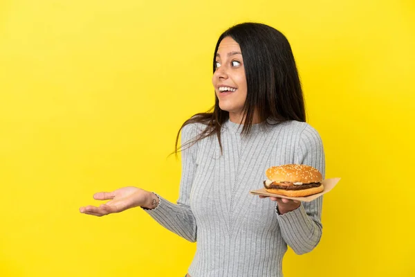 Young Caucasian Woman Holding Burger Isolated Yellow Background Surprise Expression — Stock Photo, Image
