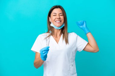 Mavi arka planda izole edilmiş orta yaşlı doktor kadın güçlü bir jest yapıyor.