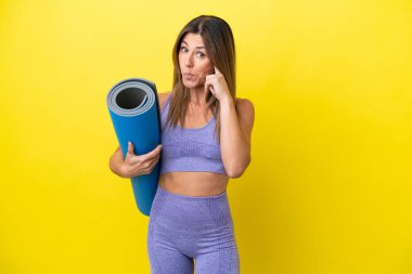 Sport woman going to yoga classes while holding a mat isolated non yellow background thinking an idea