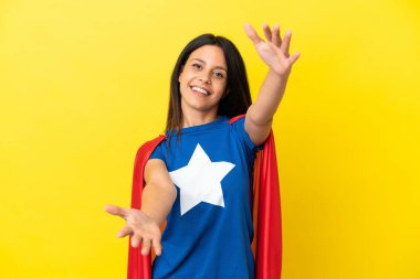 Sarı arka planda, süper kahraman kostümlü ve gelecek vadeden hareketler yapan bir kadın.