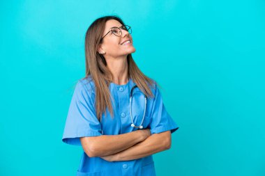 Orta yaşlı cerrah kadın mavi arka planda izole edilmiş gülümserken yukarı bakıyor