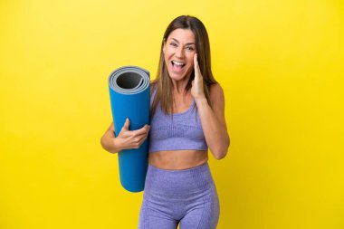 Sport woman going to yoga classes while holding a mat isolated non yellow background shouting with mouth wide open