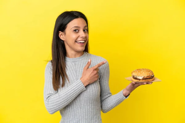 Young Caucasian Woman Holding Burger Isolated Yellow Background Pointing Finger — Stock Photo, Image