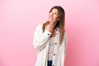 Orta yaşlı beyaz kadın pembe arka planda izole edilmiş gülümserken yukarı bakıyor.