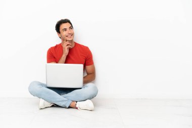 Kafkasyalı, laptoplu yakışıklı bir adam yerde oturmuş, yukarı bakarken bir fikir düşünüyor.