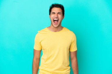 Kafkasyalı yakışıklı adam, izole edilmiş mavi arka planda, ağzı açık bir şekilde öne doğru bağırıyor.