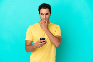 Kafkasyalı yakışıklı adam mavi arka plan üzerinde düşünüp bir mesaj gönderiyor.