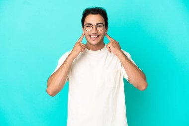 Kafkasyalı yakışıklı adam mavi arka planda mutlu ve hoş bir ifadeyle gülümsüyor.