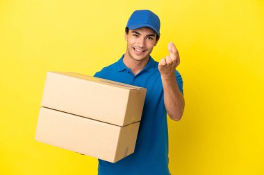 Delivery man over isolated yellow wall making money gesture
