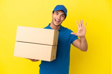 Delivery man over isolated yellow wall counting five with fingers